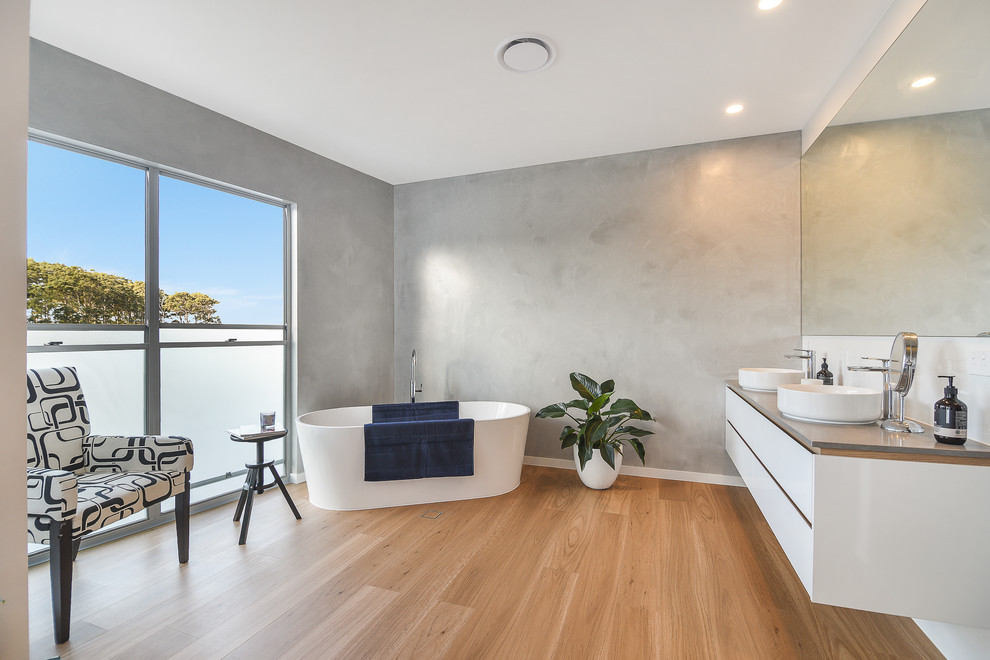 This is an example of a contemporary bathroom in Sunshine Coast with flat-panel cabinets, white cabinets, a freestanding tub, grey walls, medium hardwood floors, a vessel sink, brown floor and grey benchtops.