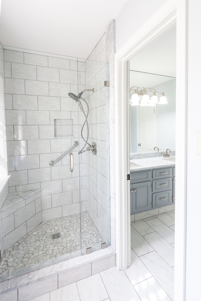Example of a transitional master white tile and subway tile porcelain tile and white floor freestanding bathtub design with raised-panel cabinets, gray cabinets, white walls, an undermount sink, marble countertops and a hinged shower door