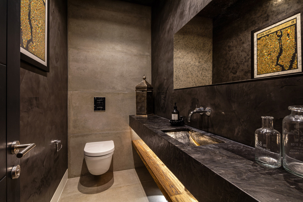 This is an example of a mid-sized mediterranean powder room in West Midlands with a wall-mount toilet, black walls, concrete floors, a wall-mount sink and grey floor.