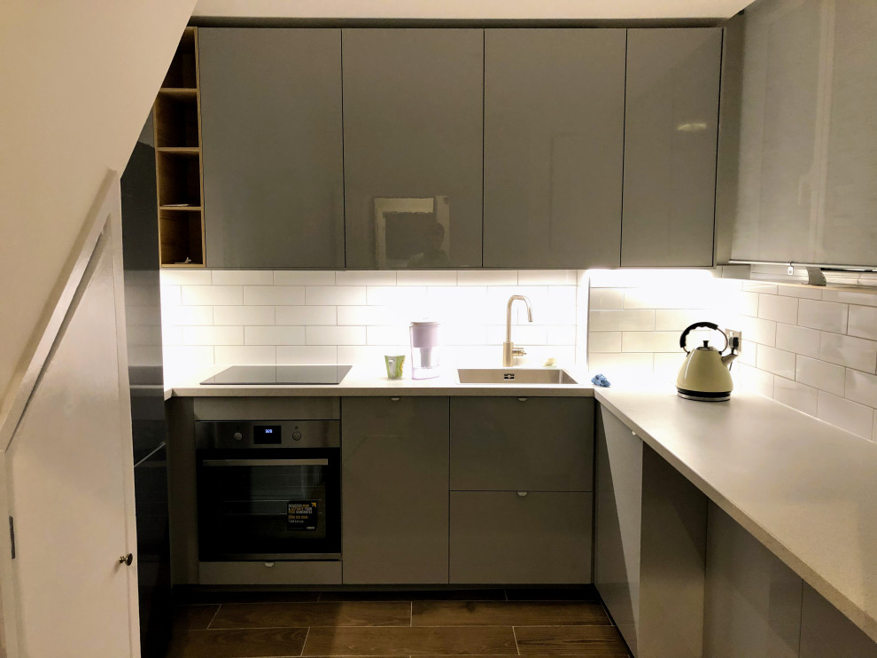 Inspiration for a mid-sized modern u-shaped eat-in kitchen in London with an integrated sink, flat-panel cabinets, white cabinets, laminate benchtops, white splashback, ceramic splashback, black appliances, ceramic floors, a peninsula, brown floor, beige benchtop and recessed.