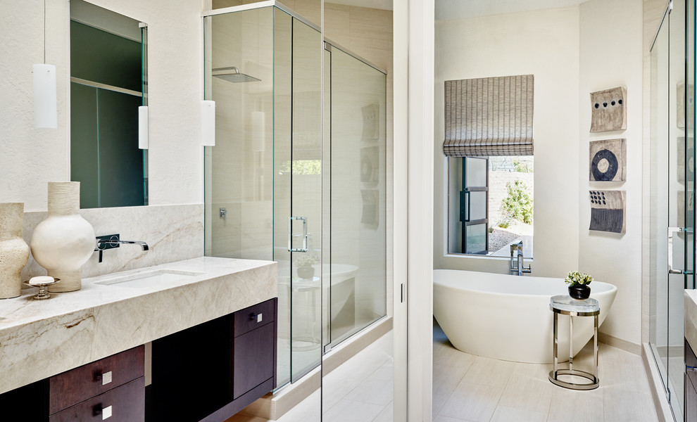 This is an example of a large contemporary master bathroom in Phoenix with recessed-panel cabinets, dark wood cabinets, a freestanding tub, a corner shower, a two-piece toilet, white tile, stone tile, white walls, marble floors, an undermount sink and quartzite benchtops.