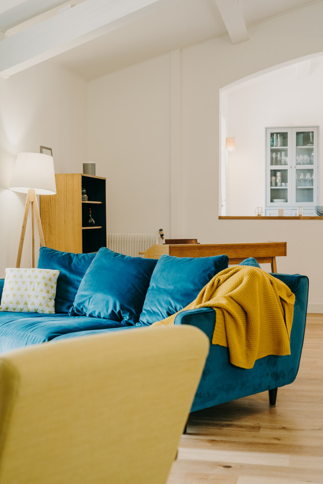 Idée de décoration pour un grand salon ouvert avec un mur bleu, parquet clair, un poêle à bois, un téléviseur fixé au mur, un sol beige, poutres apparentes et un plafond cathédrale.