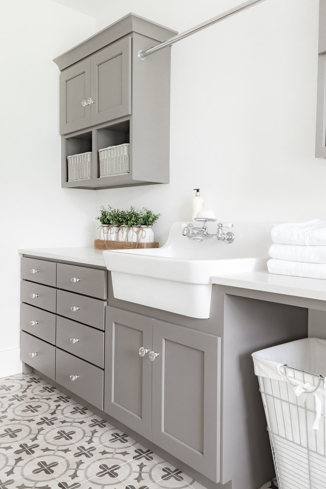 Mid-sized country galley dedicated laundry room in Philadelphia with a farmhouse sink, shaker cabinets, grey cabinets, quartz benchtops, white walls, porcelain floors, grey floor and white benchtop.