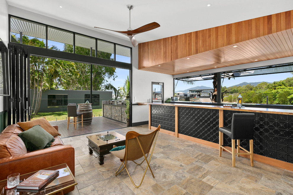 This is an example of a large tropical galley seated home bar in Cairns with black cabinets, a drop-in sink, open cabinets, granite benchtops, travertine floors and black benchtop.