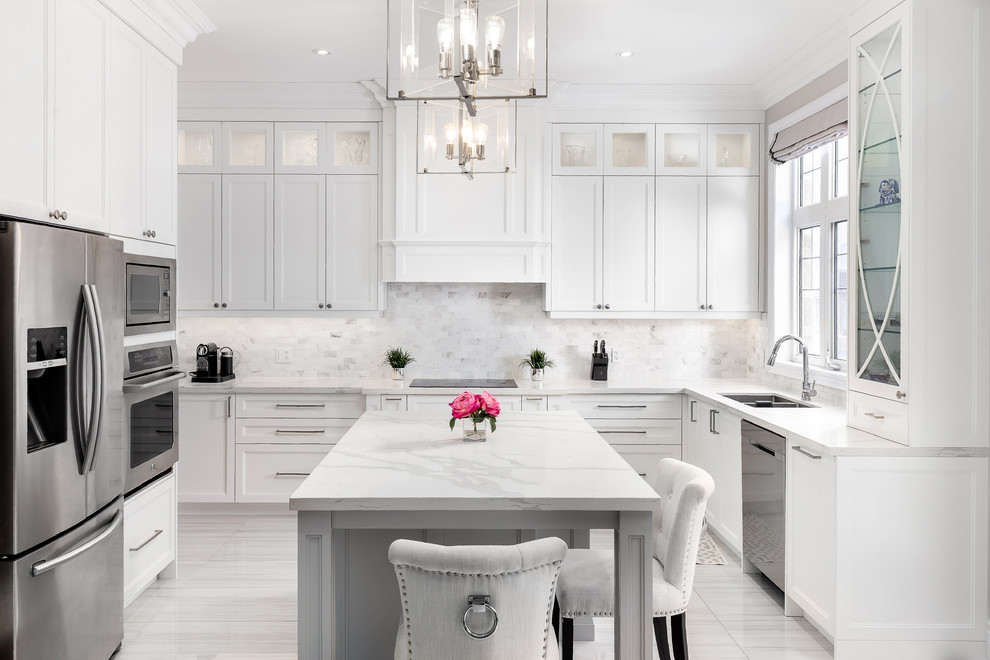 This is an example of a large transitional u-shaped open plan kitchen in Toronto with an undermount sink, shaker cabinets, white cabinets, quartz benchtops, grey splashback, mosaic tile splashback, stainless steel appliances, ceramic floors, with island, grey floor and white benchtop.