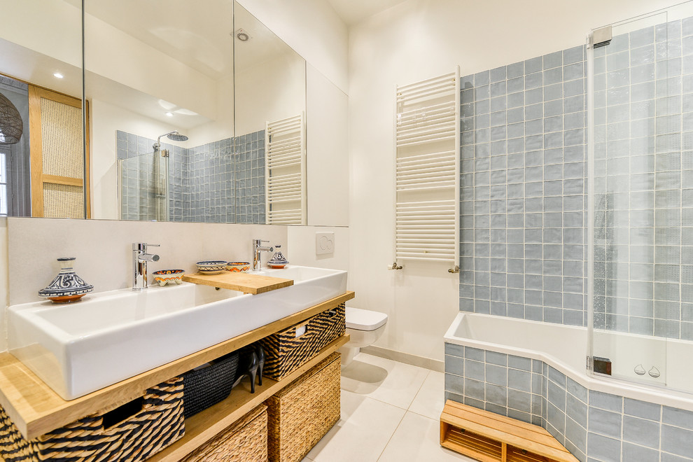 This is an example of a mid-sized contemporary master bathroom in Paris with a wall-mount toilet, wood benchtops, open cabinets, a corner tub, a shower/bathtub combo, white walls, an open shower, white cabinets, blue tile, ceramic floors, a drop-in sink and beige floor.