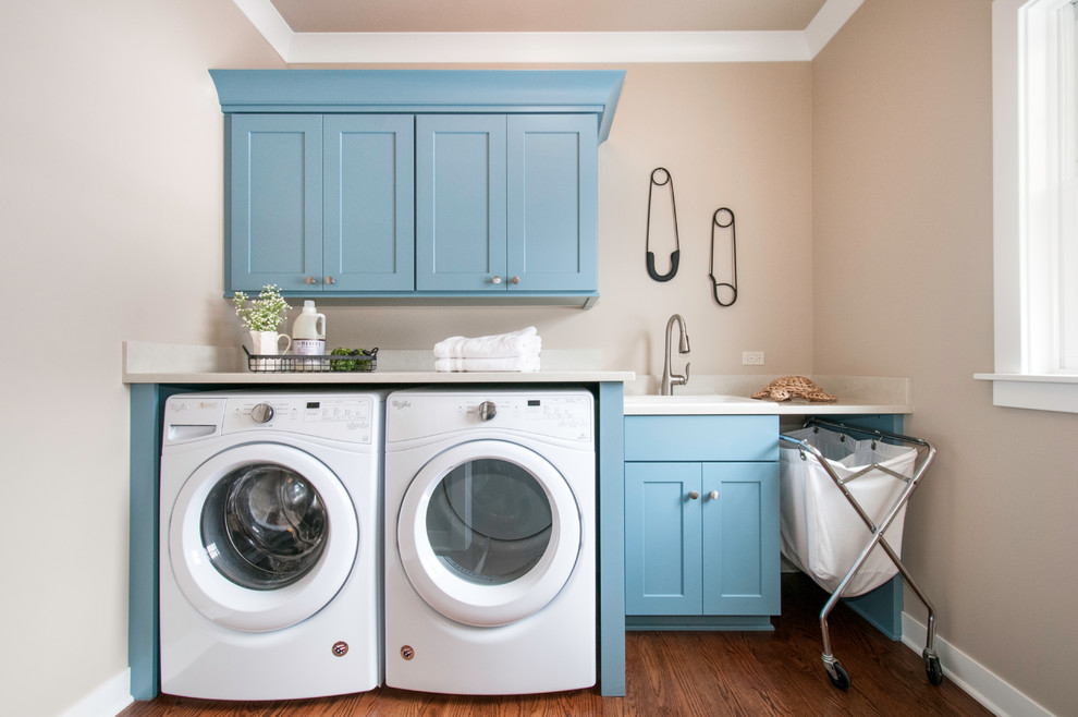 Small transitional single-wall dedicated laundry room in Chicago with shaker cabinets, blue cabinets, quartz benchtops, beige walls, medium hardwood floors, a side-by-side washer and dryer, a drop-in sink, brown floor and white benchtop.