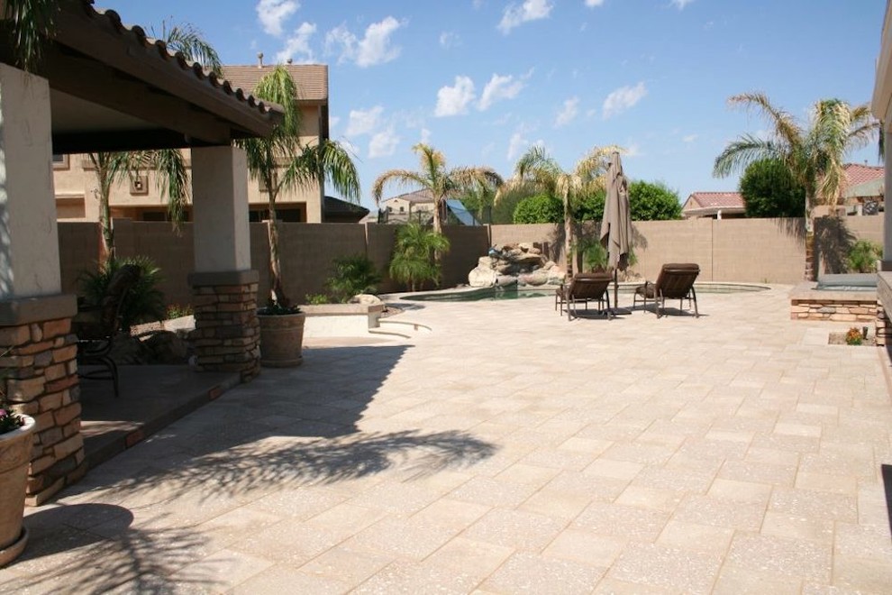 This is an example of a large tropical backyard patio in Phoenix with a fire feature and natural stone pavers.