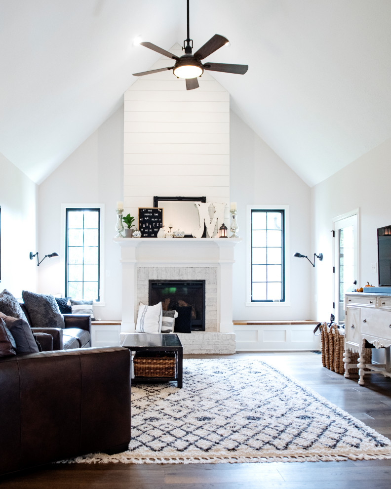 Cottage enclosed medium tone wood floor, brown floor, vaulted ceiling and shiplap wall living room photo in Indianapolis with white walls, a standard fireplace, a stone fireplace and a wall-mounted tv