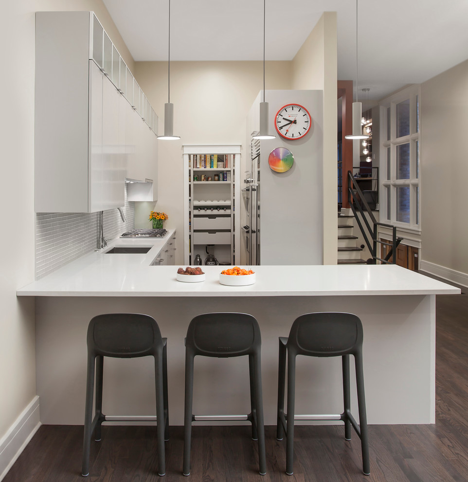 Mid-sized contemporary l-shaped kitchen in Chicago with an undermount sink, flat-panel cabinets, white cabinets, quartz benchtops, grey splashback, glass tile splashback, stainless steel appliances, dark hardwood floors, a peninsula and grey floor.