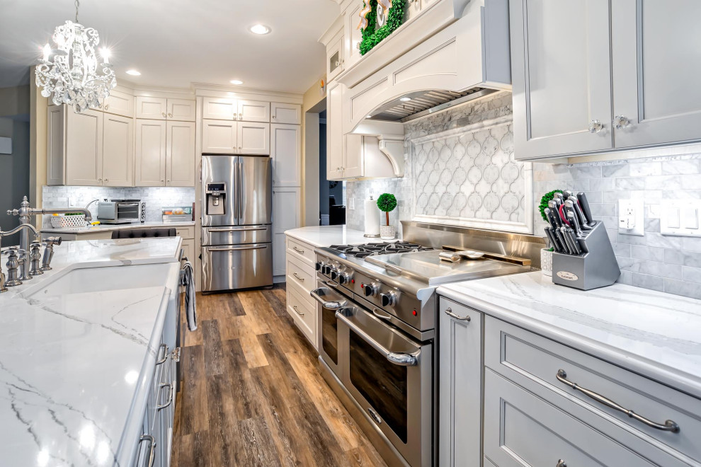 Inspiration for a large transitional single-wall medium tone wood floor and brown floor eat-in kitchen remodel in Philadelphia with a farmhouse sink, shaker cabinets, white cabinets, quartz countertops, gray backsplash, porcelain backsplash, stainless steel appliances, an island and white countertops