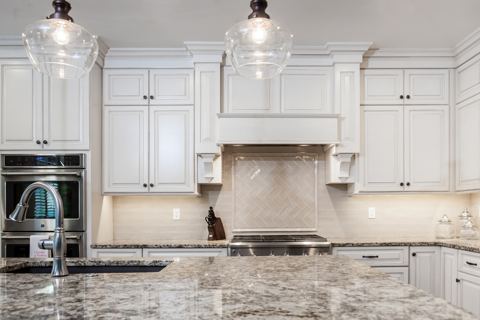 Large transitional l-shaped kitchen photo in St Louis with an undermount sink, raised-panel cabinets, white cabinets, granite countertops, beige backsplash, subway tile backsplash, stainless steel appliances and an island