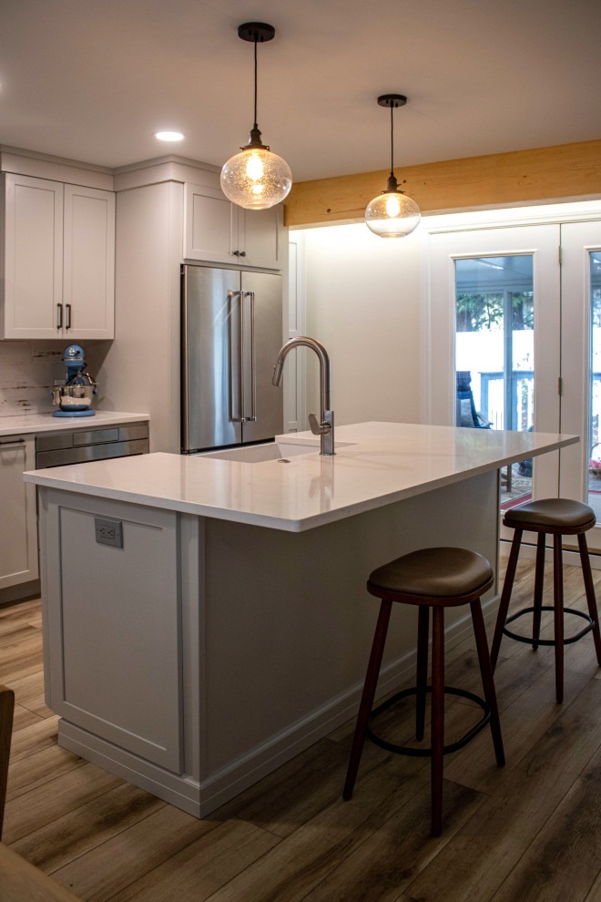 This is an example of a large transitional l-shaped eat-in kitchen in Cleveland with an undermount sink, shaker cabinets, grey cabinets, quartz benchtops, white splashback, ceramic splashback, stainless steel appliances, vinyl floors, with island, brown floor and white benchtop.