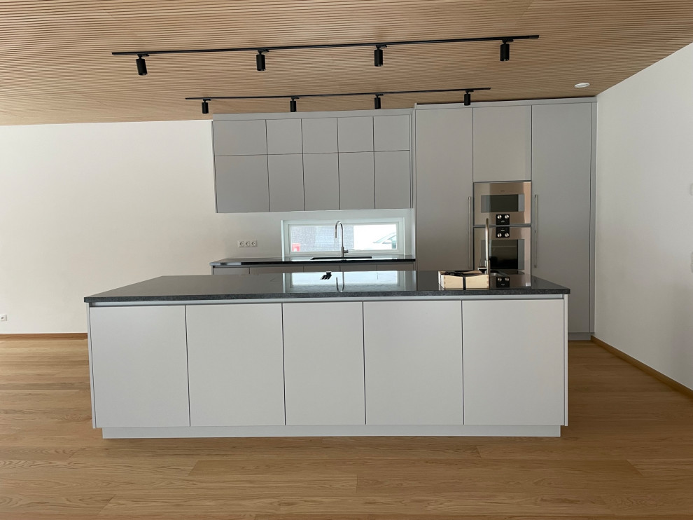Eat-in kitchen - mid-sized modern galley light wood floor and wood ceiling eat-in kitchen idea in Malmo with an undermount sink, flat-panel cabinets, gray cabinets, granite countertops, white backsplash, window backsplash, stainless steel appliances, an island and gray countertops