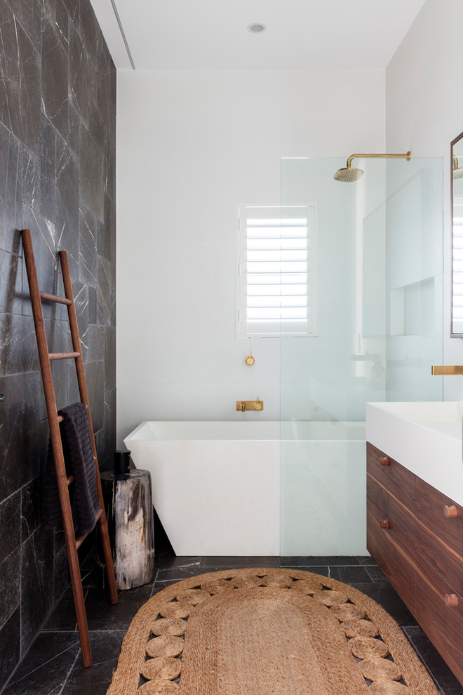 Inspiration for a mid-sized contemporary master bathroom in Sydney with furniture-like cabinets, dark wood cabinets, a freestanding tub, a shower/bathtub combo, a wall-mount toilet, white tile, ceramic tile, grey walls, limestone floors, an integrated sink, solid surface benchtops and grey floor.