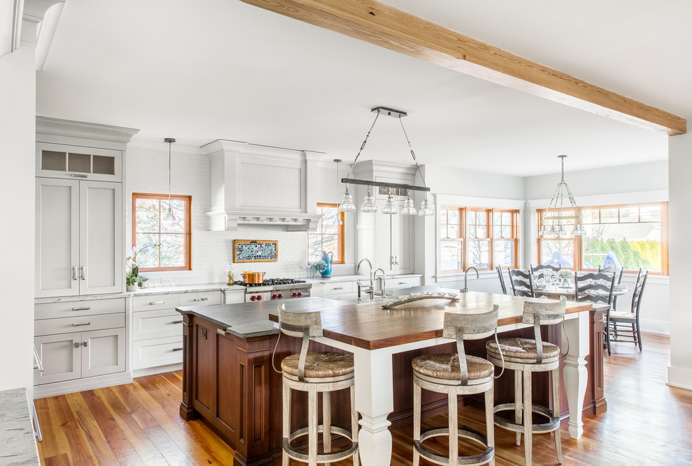 This is an example of a beach style eat-in kitchen in Other with shaker cabinets, white cabinets, white splashback, subway tile splashback, stainless steel appliances, medium hardwood floors and multiple islands.