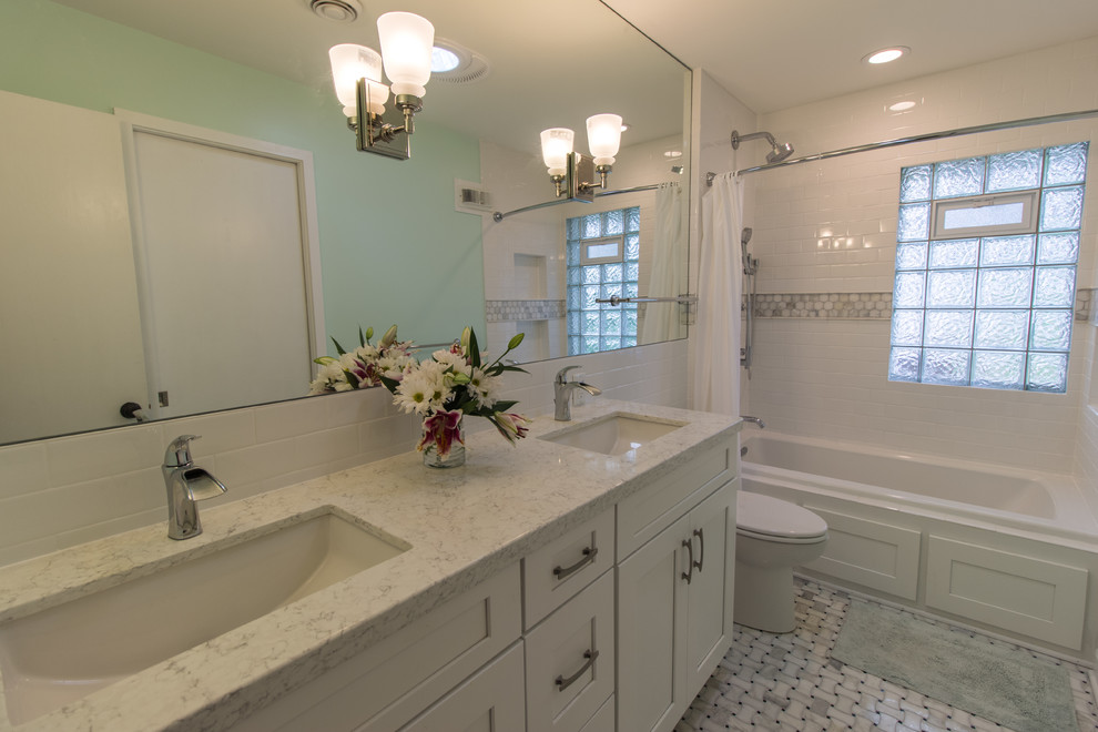 This is an example of a mid-sized transitional master bathroom in Minneapolis with recessed-panel cabinets, white cabinets, an alcove tub, a shower/bathtub combo, a one-piece toilet, white tile, subway tile, blue walls, marble floors, an undermount sink, engineered quartz benchtops, white floor, a shower curtain and white benchtops.