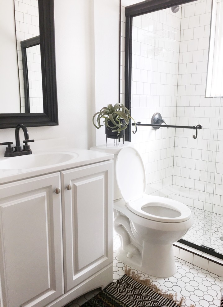 This is an example of a small transitional bathroom in Denver with raised-panel cabinets, white cabinets, an alcove shower, a one-piece toilet, white tile, ceramic tile, white walls, mosaic tile floors, an integrated sink, solid surface benchtops, white floor, a sliding shower screen and white benchtops.