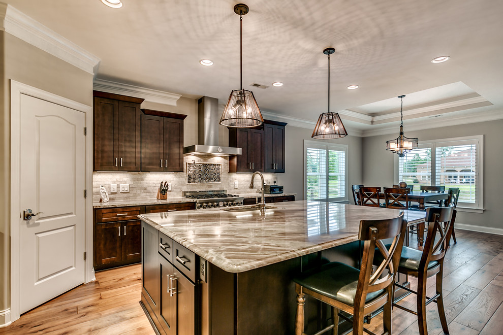 Open concept kitchen - large transitional l-shaped medium tone wood floor and brown floor open concept kitchen idea with an undermount sink, shaker cabinets, dark wood cabinets, granite countertops, gray backsplash, stone tile backsplash, stainless steel appliances, an island and gray countertops