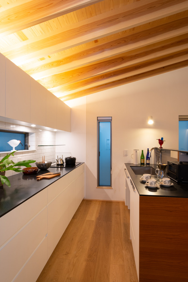 Photo of a contemporary galley open plan kitchen in Other with an undermount sink, flat-panel cabinets, white cabinets, solid surface benchtops, white splashback, panelled appliances, medium hardwood floors, a peninsula, brown floor and black benchtop.
