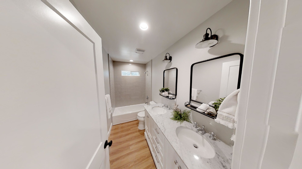 This is an example of a mid-sized country kids bathroom in Sacramento with recessed-panel cabinets, white cabinets, an open shower, a two-piece toilet, gray tile, ceramic tile, grey walls, laminate floors, an undermount sink, quartzite benchtops, brown floor, an open shower and white benchtops.