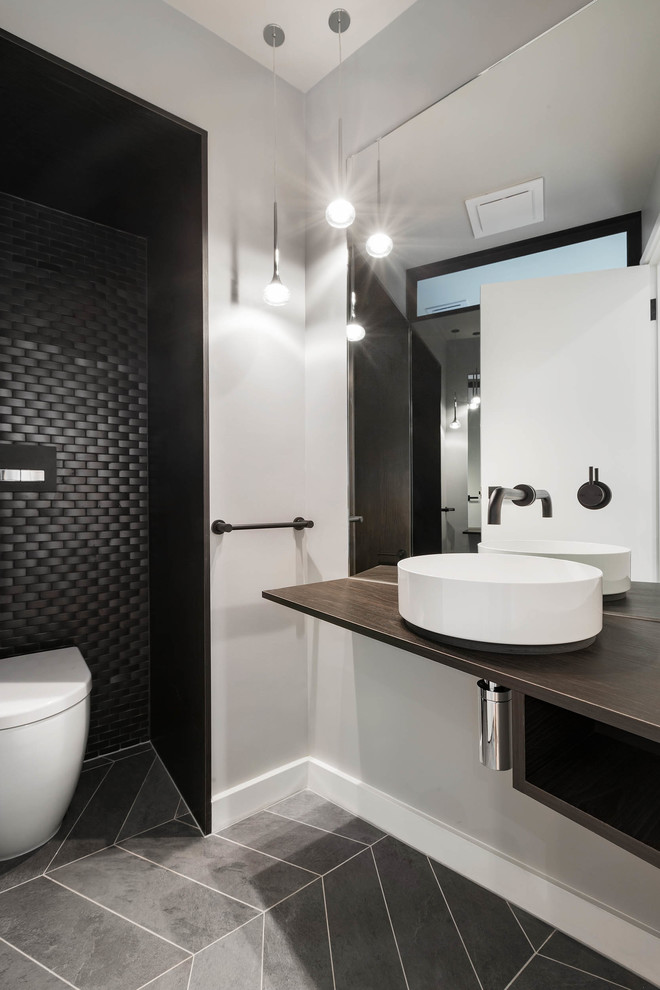This is an example of a contemporary bathroom in Melbourne with open cabinets, dark wood cabinets, a wall-mount toilet, black tile, mosaic tile, grey walls, a vessel sink, wood benchtops, grey floor and brown benchtops.