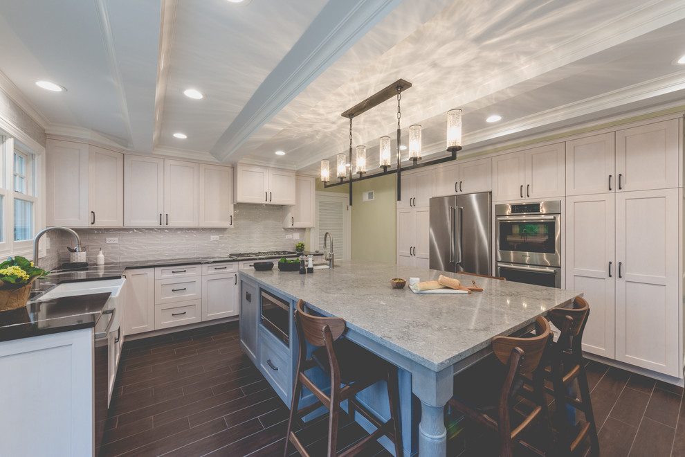 Mid-sized transitional kitchen in Chicago with a farmhouse sink, shaker cabinets, grey cabinets, quartz benchtops, grey splashback, ceramic splashback, stainless steel appliances, porcelain floors, with island, brown floor and black benchtop.