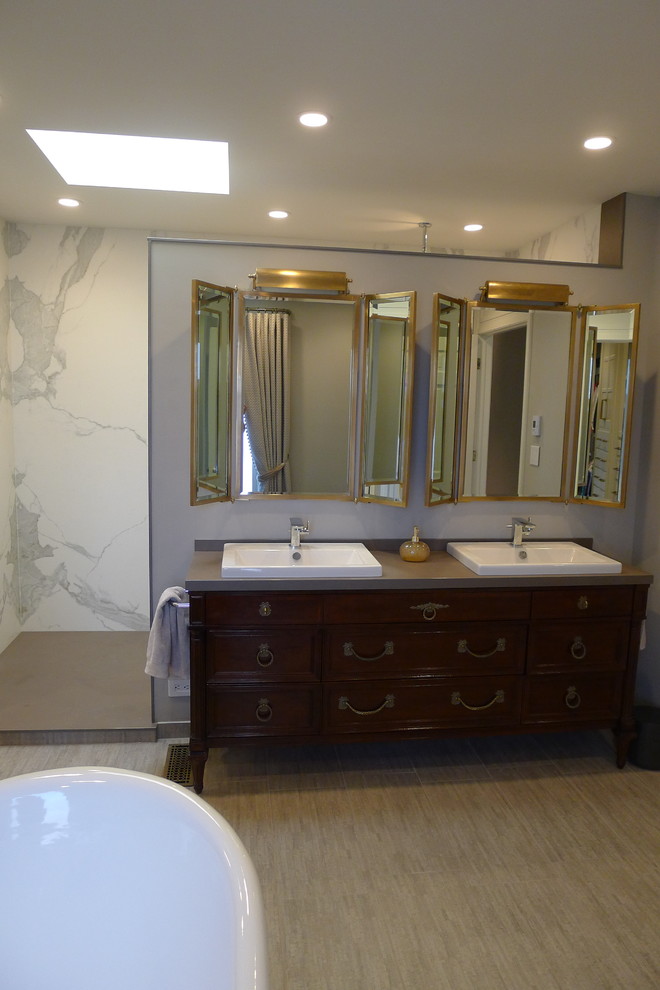 This is an example of a large transitional master bathroom in Indianapolis with a drop-in sink, furniture-like cabinets, dark wood cabinets, solid surface benchtops, a freestanding tub, an open shower, a one-piece toilet, gray tile, porcelain tile, grey walls and porcelain floors.