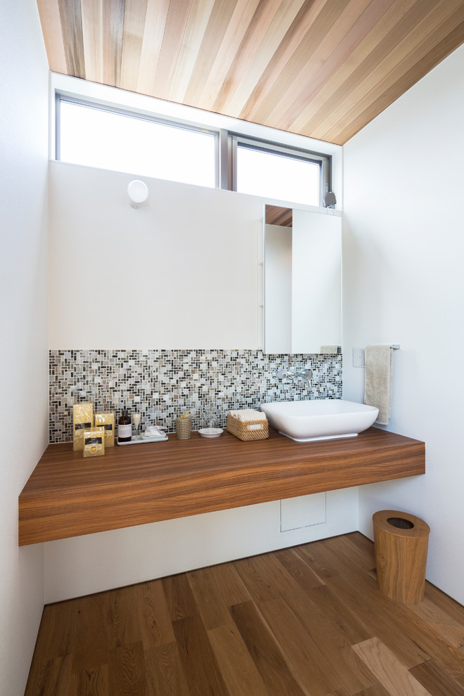 This is an example of a contemporary powder room in Other with white walls, medium hardwood floors, a vessel sink, wood benchtops, brown floor and brown benchtops.