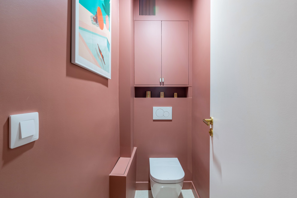 Cette image montre un WC suspendu minimaliste de taille moyenne avec un placard à porte affleurante, des portes de placard violettes, un mur rose, un sol en terrazzo, un sol blanc et meuble-lavabo encastré.