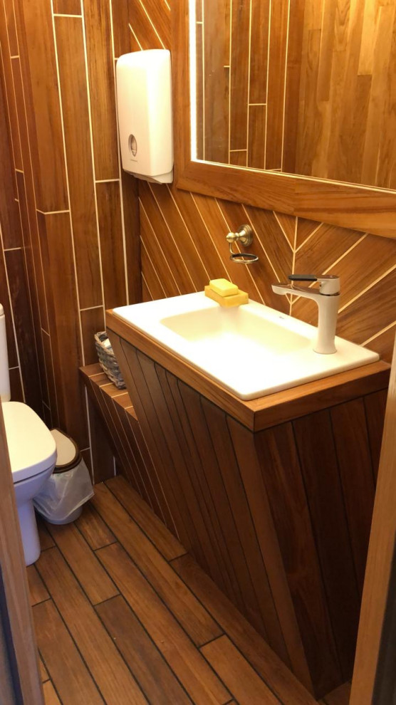 Idéer för små industriella gult toaletter, med bruna skåp, en toalettstol med hel cisternkåpa, bruna väggar, mörkt trägolv, ett undermonterad handfat, träbänkskiva och gult golv