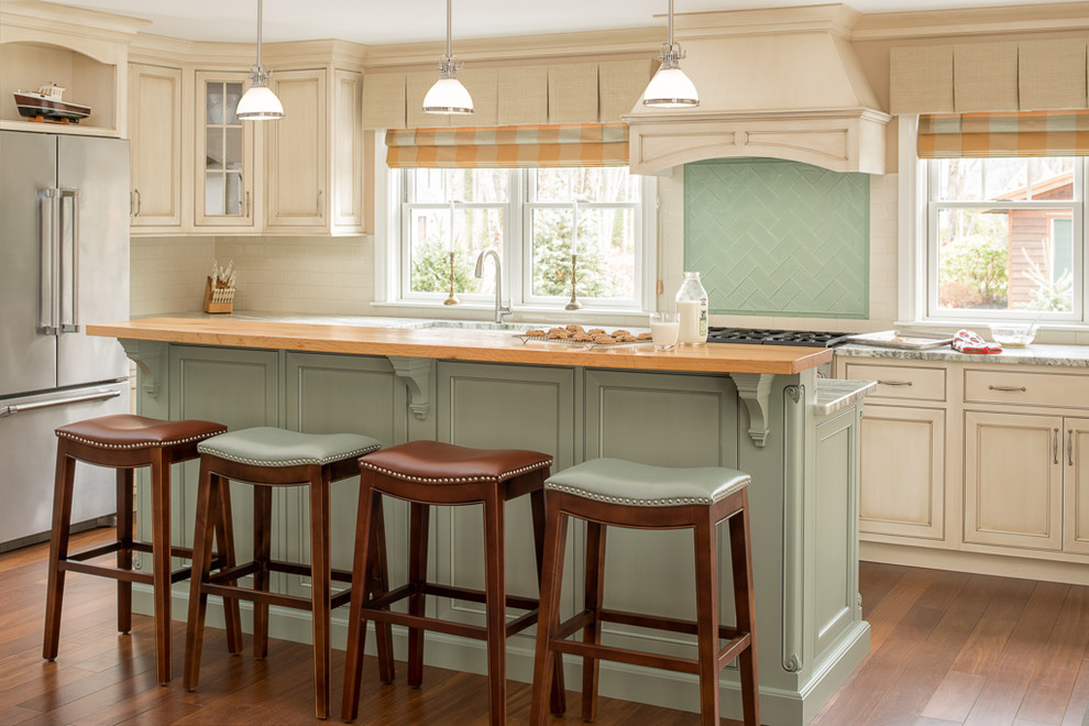 Design ideas for a traditional u-shaped separate kitchen in Portland Maine with with island, beaded inset cabinets, beige cabinets, green splashback, glass tile splashback, stainless steel appliances, medium hardwood floors, a farmhouse sink and brown floor.