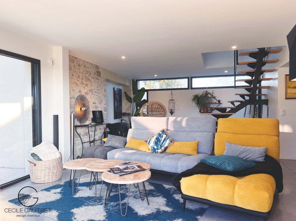Modernes Wohnzimmer mit weißer Wandfarbe, Betonboden, Kaminofen, Eck-TV, grauem Boden und Steinwänden in Nantes