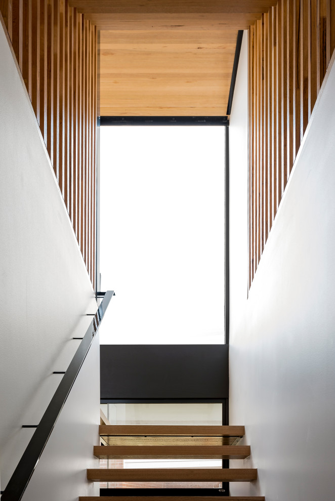 This is an example of a large contemporary wood floating staircase in Melbourne with open risers, metal railing and wood walls.