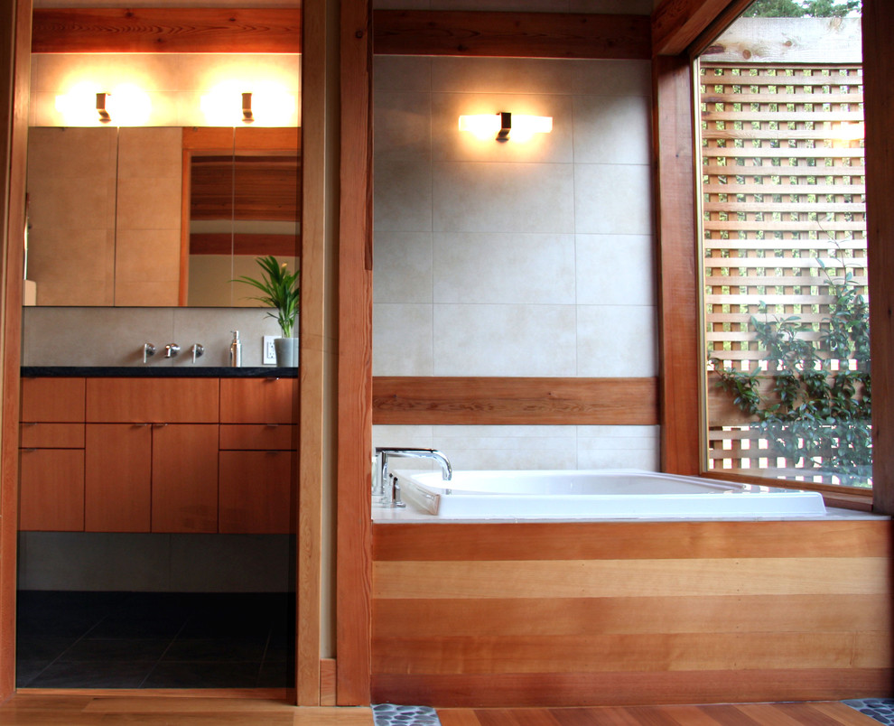 This is an example of a mid-sized asian master bathroom in Vancouver with flat-panel cabinets, medium wood cabinets, a corner tub, beige tile, ceramic tile, medium hardwood floors, an undermount sink and black benchtops.