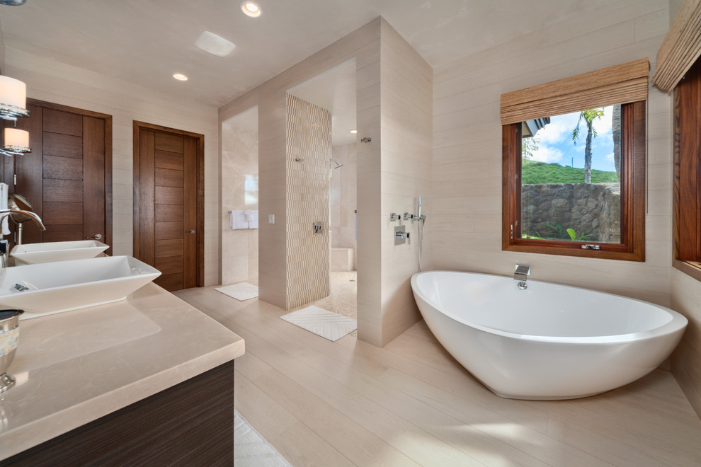 Inspiration for a large contemporary master bathroom in Hawaii with porcelain floors, flat-panel cabinets, dark wood cabinets, a freestanding tub, an open shower, beige tile, porcelain tile, beige walls, a vessel sink, limestone benchtops, beige floor and an open shower.