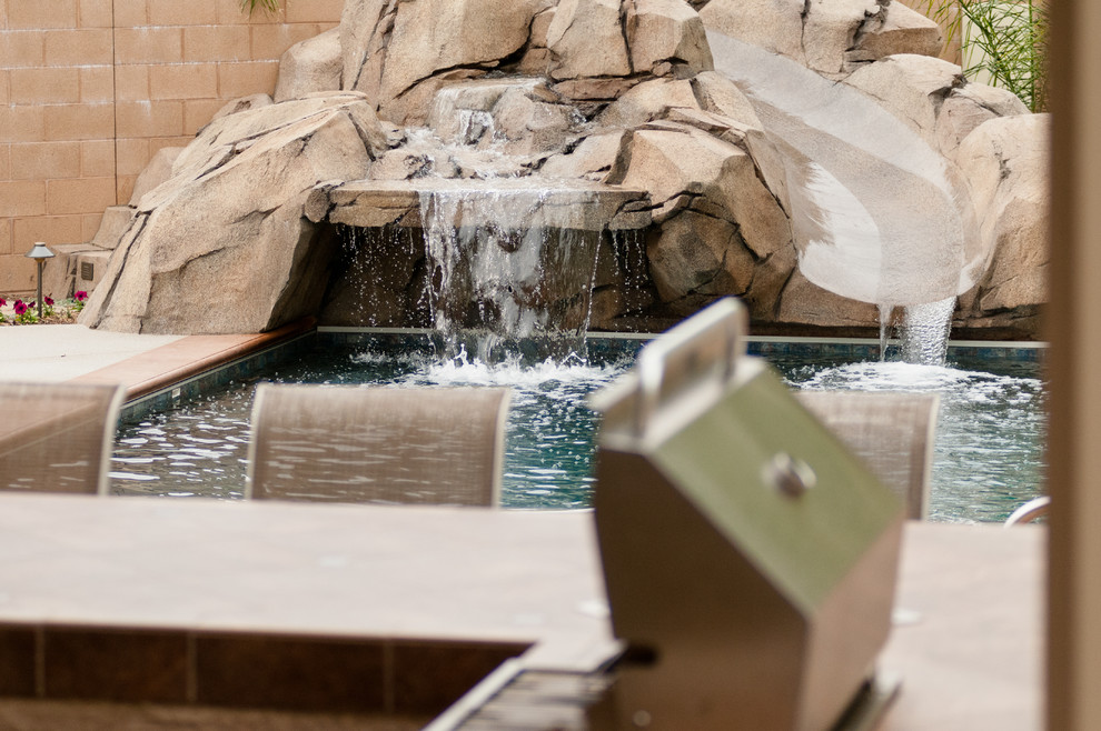 Diseño de piscina con tobogán alargada exótica de tamaño medio rectangular en patio trasero con losas de hormigón