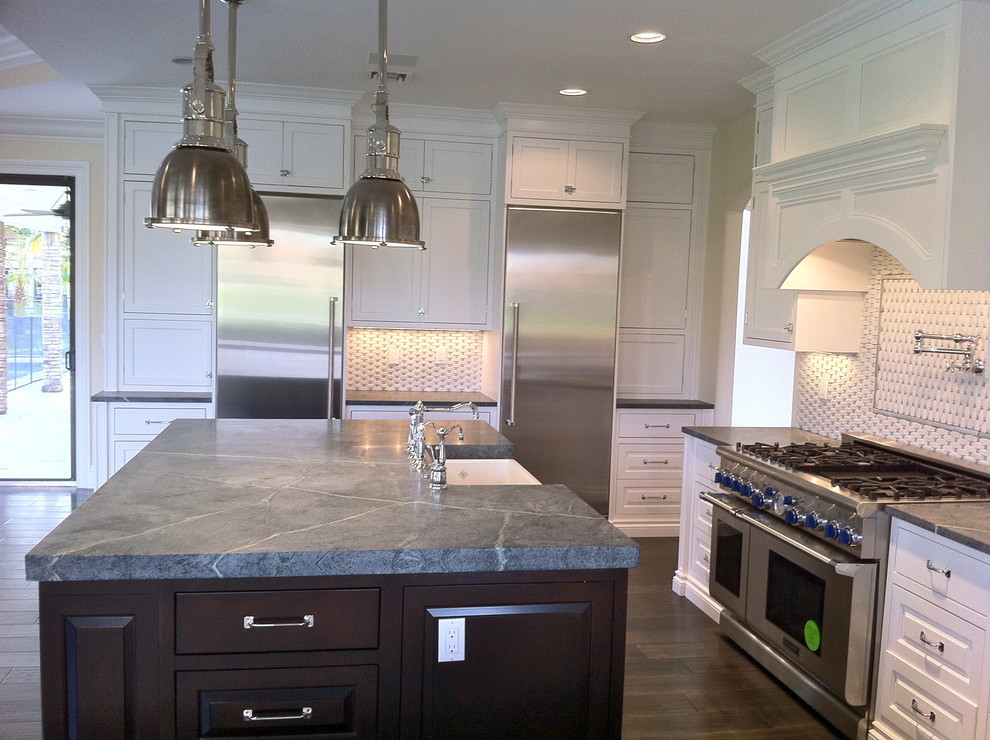 Example of a large transitional u-shaped dark wood floor and brown floor open concept kitchen design in Miami with a farmhouse sink, shaker cabinets, white cabinets, granite countertops, multicolored backsplash, stone tile backsplash, stainless steel appliances and an island