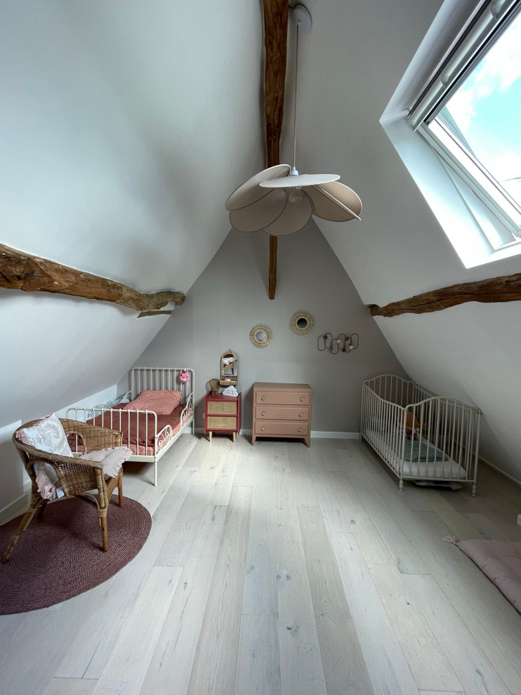 This is an example of a large scandi toddler’s room for girls in Paris with beige walls, light hardwood flooring, beige floors, exposed beams and wood walls.