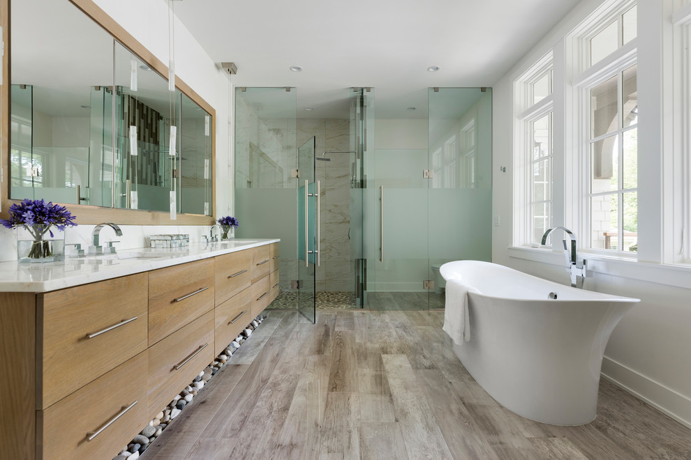 Country bathroom in Minneapolis with flat-panel cabinets, medium wood cabinets, a freestanding tub, a curbless shower, beige tile, white walls, an undermount sink, grey floor, a hinged shower door and white benchtops.