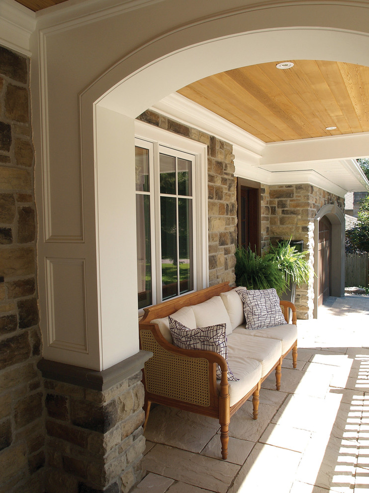 Large traditional front yard verandah in Toronto with natural stone pavers, a roof extension and a container garden.