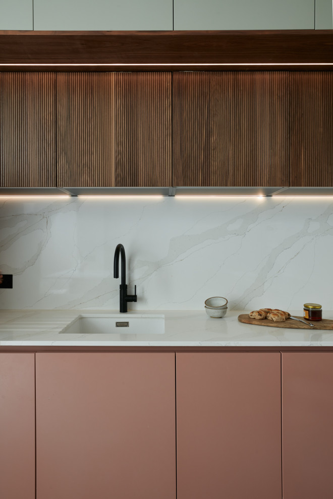 This is an example of a small contemporary l-shaped eat-in kitchen in London with an integrated sink, louvered cabinets, red cabinets, quartzite benchtops, beige splashback, engineered quartz splashback, black appliances, ceramic floors, with island, brown floor and beige benchtop.