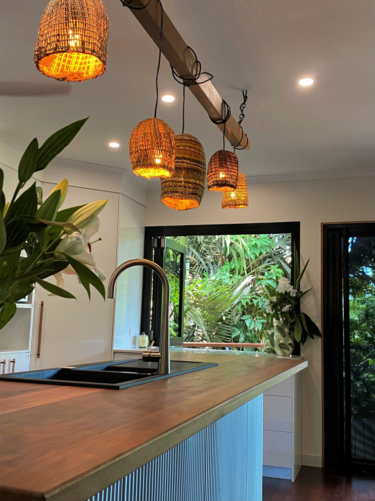 Esempio di un cucina con isola centrale tropicale con lavello a doppia vasca, ante bianche, top in legno, paraspruzzi verde, parquet scuro e top bianco