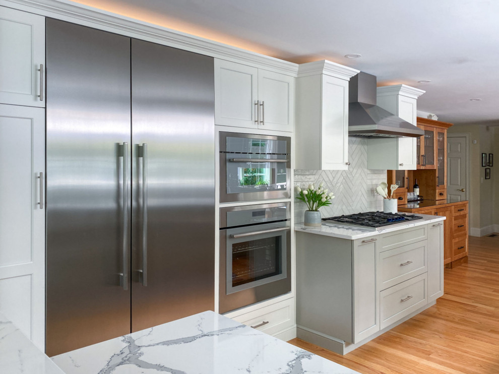 Example of a transitional galley medium tone wood floor kitchen design in Boston with an undermount sink, shaker cabinets, white cabinets, quartz countertops, white backsplash, ceramic backsplash, stainless steel appliances, no island and white countertops