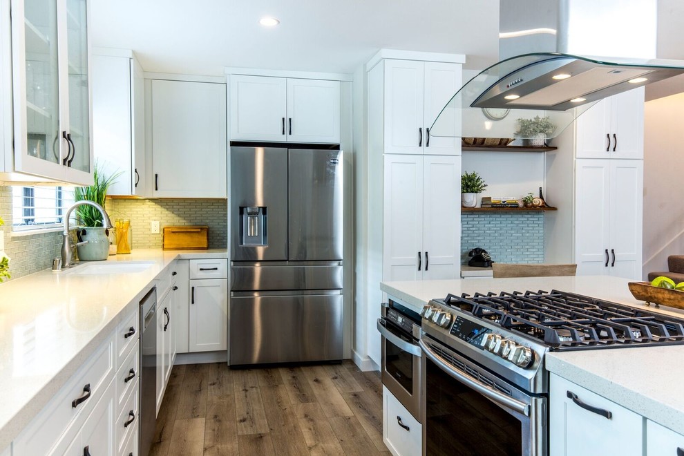 Photo of a mid-sized transitional l-shaped open plan kitchen in Los Angeles with an undermount sink, shaker cabinets, white cabinets, quartz benchtops, blue splashback, glass tile splashback, stainless steel appliances, medium hardwood floors, with island, brown floor and white benchtop.