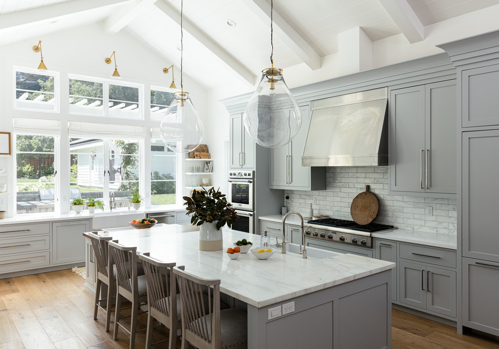 Inspiration for a large transitional l-shaped kitchen in San Francisco with marble benchtops, stainless steel appliances, medium hardwood floors, with island, a farmhouse sink, shaker cabinets, grey cabinets, white splashback, marble splashback and white benchtop.