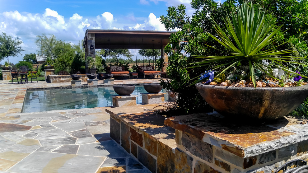 This is an example of a large traditional backyard rectangular lap pool in Dallas with a water feature and natural stone pavers.