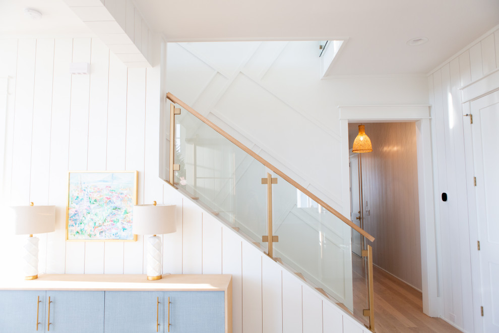 This is an example of a large beach style wood straight staircase in Charleston with wood risers, glass railing and planked wall panelling.