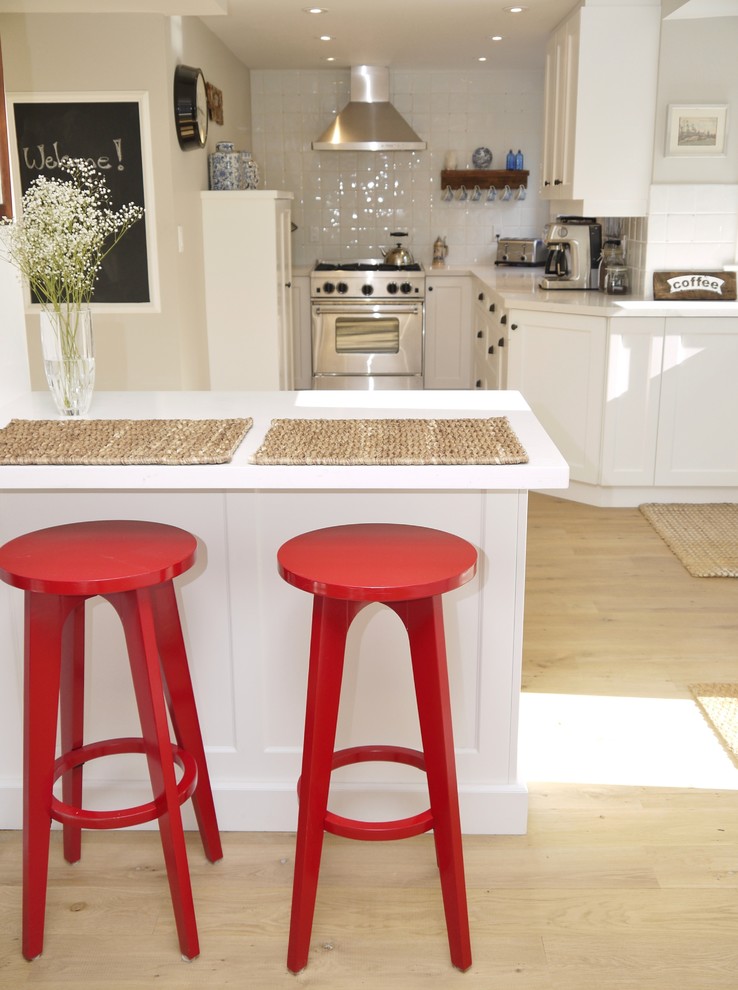 Example of a small transitional l-shaped light wood floor eat-in kitchen design in Toronto with a farmhouse sink, shaker cabinets, white cabinets, quartz countertops, white backsplash, ceramic backsplash, stainless steel appliances and a peninsula