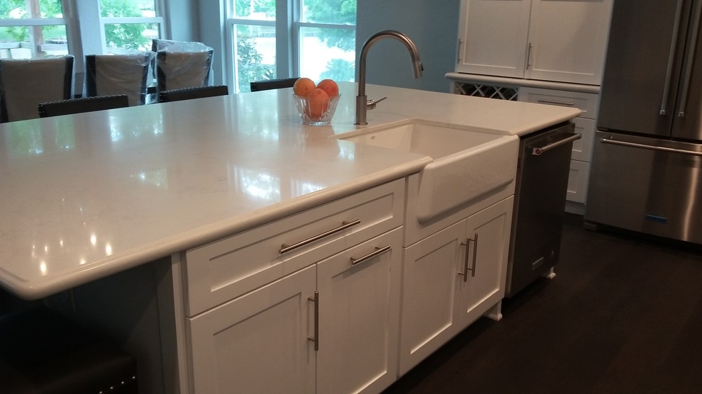 Example of a large transitional l-shaped medium tone wood floor and brown floor open concept kitchen design in Houston with a farmhouse sink, shaker cabinets, white cabinets, quartz countertops, white backsplash, marble backsplash, stainless steel appliances and an island